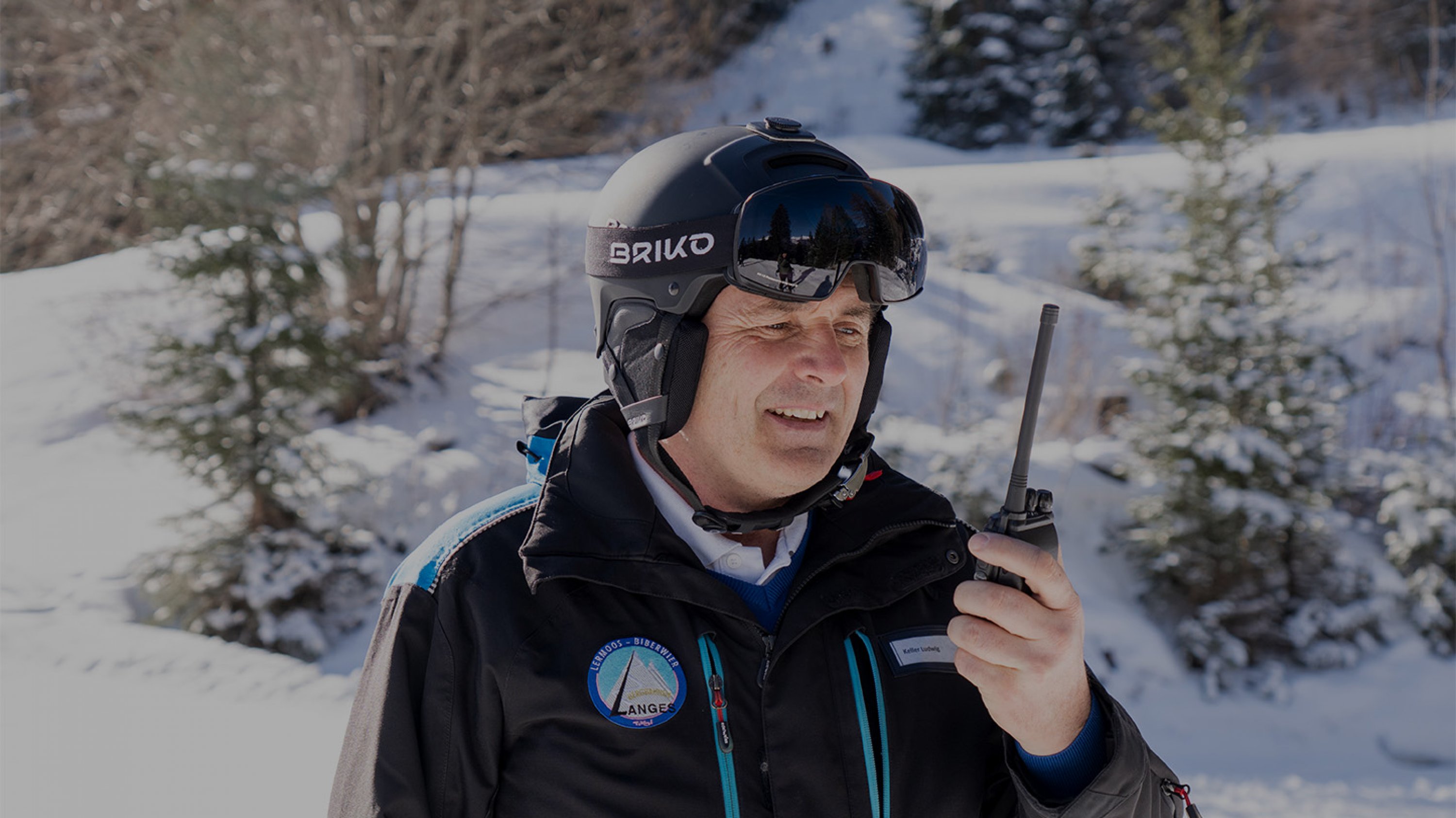 Ein Bergbahn Mitarbeiter mit einem Skihelm und einer Skibrille spricht in ein Walkie Talkie