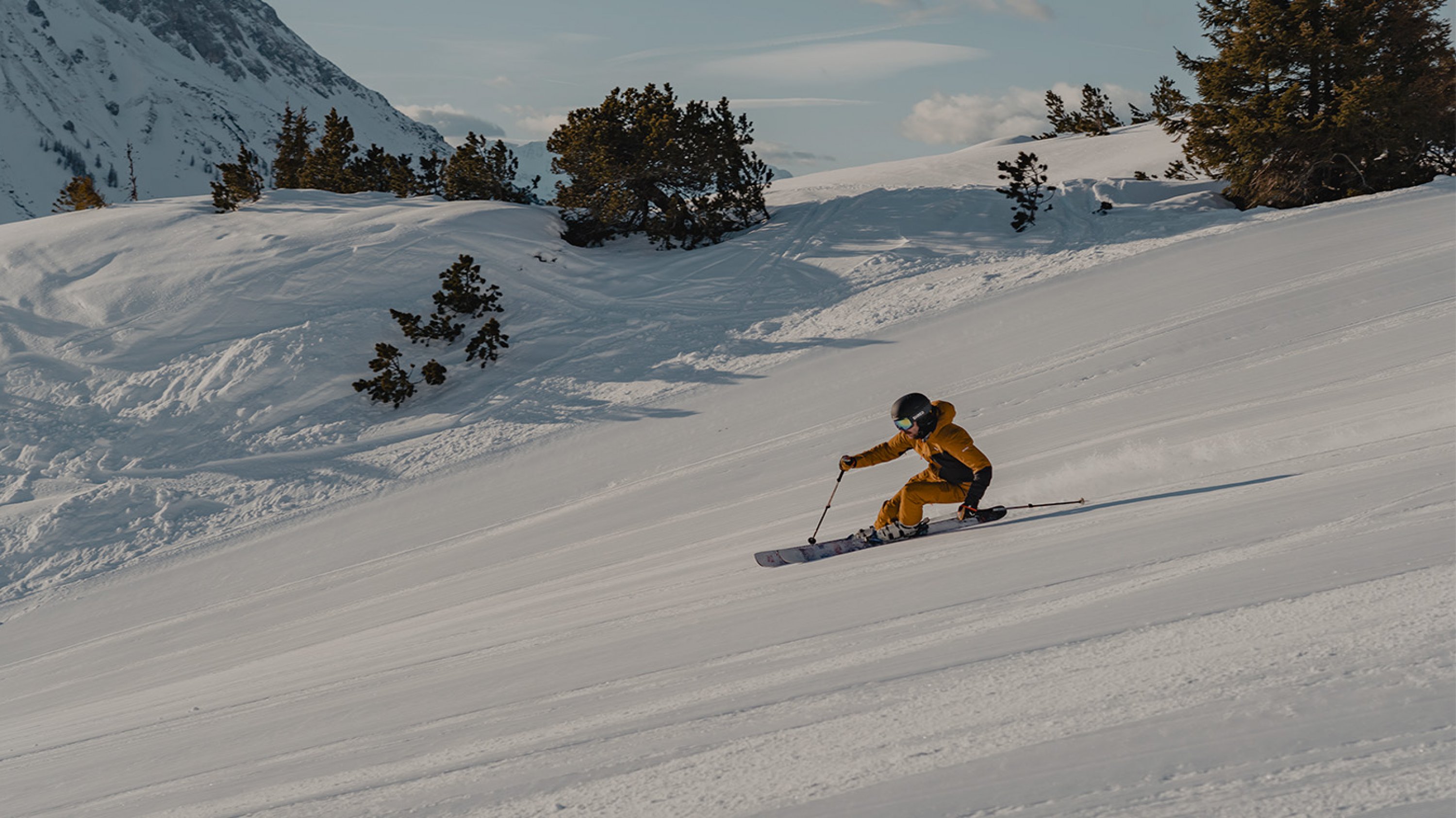 A skier makes a sporty turn with a large banking angle on a freshly groomed slope