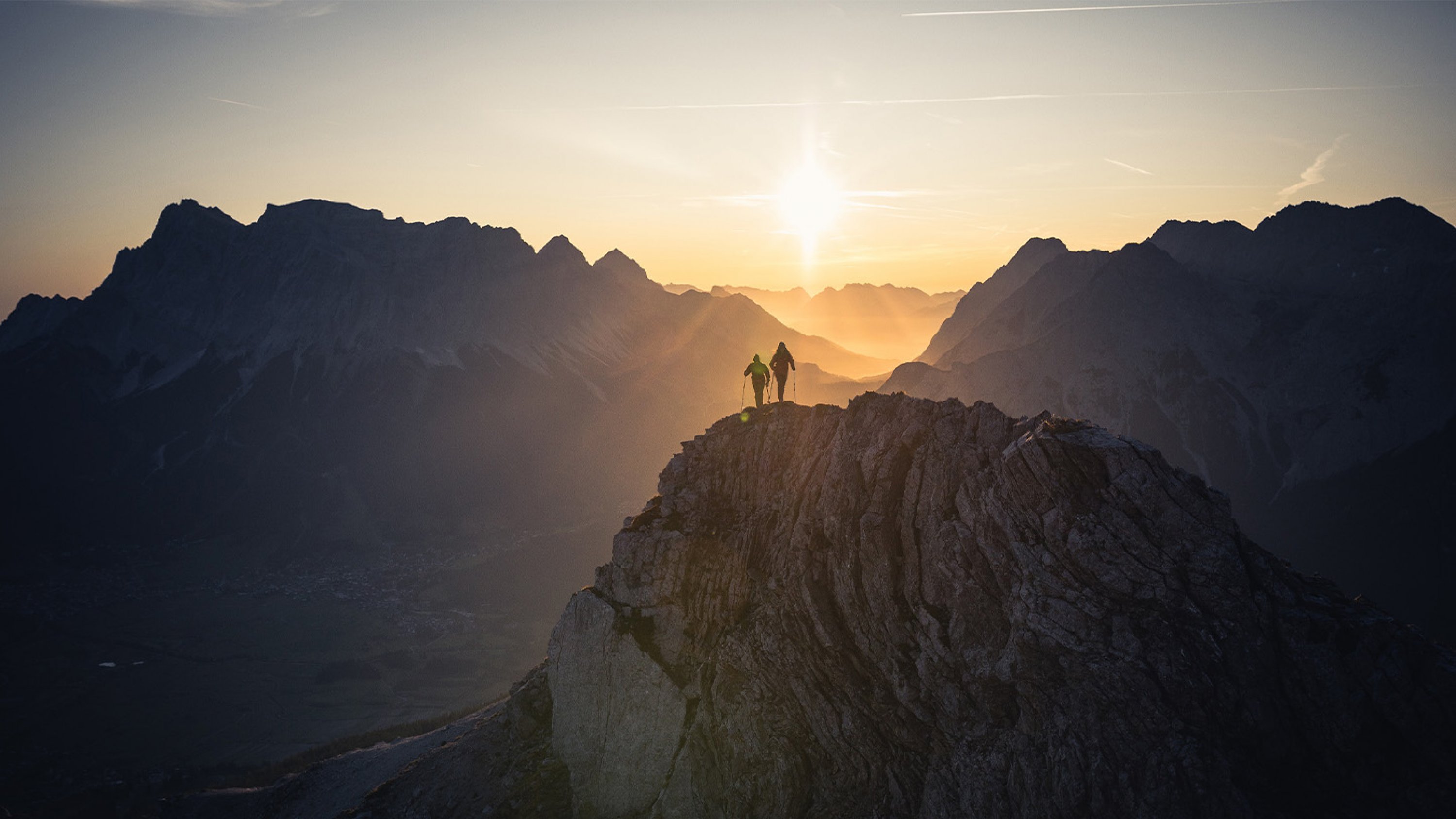 Zwei Wanderer im Sonnenaufgang, im Hintergrund Bergpanorama mit der Zugspitze