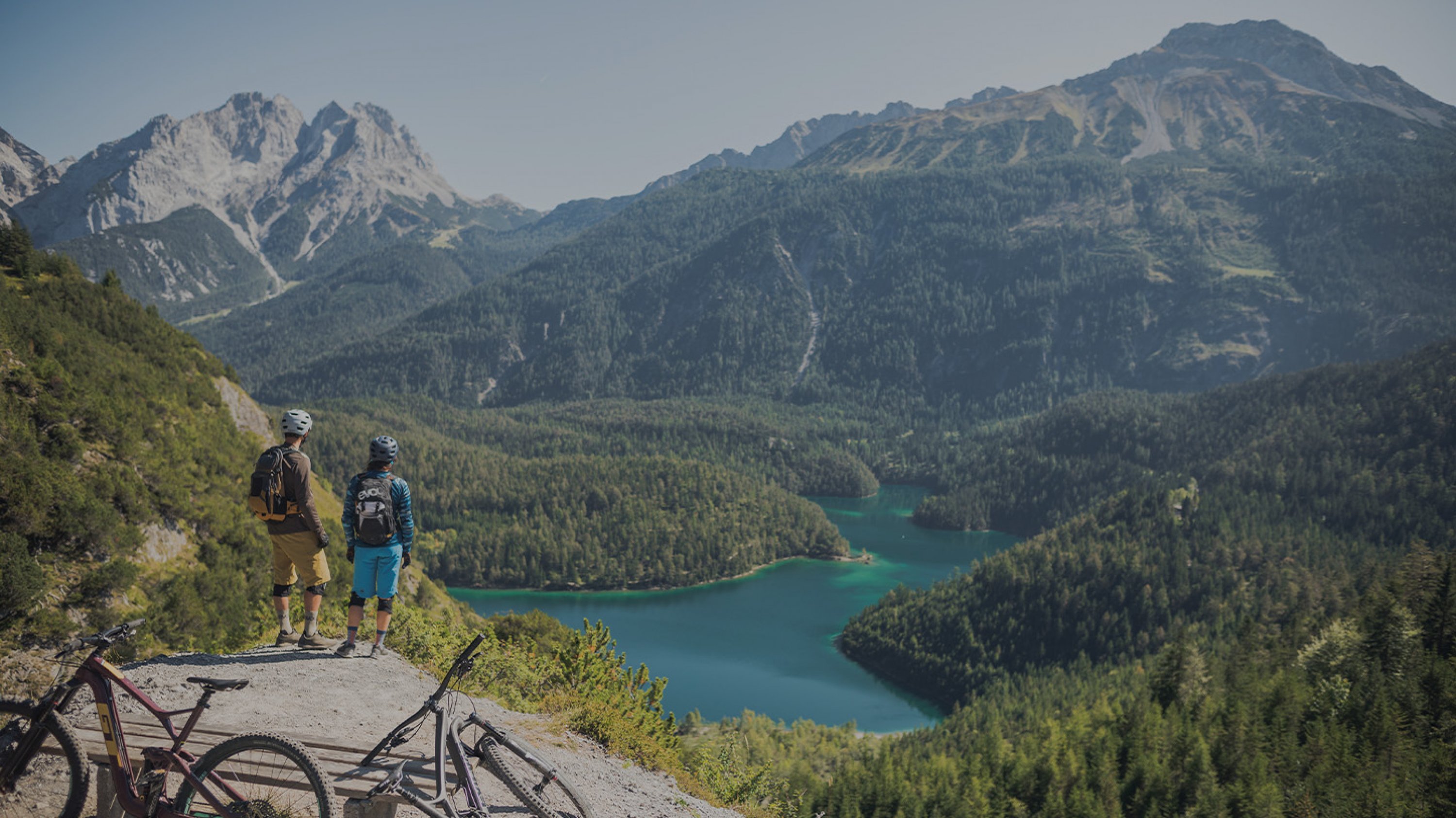 Zwei Mountainbike Fahrer schauen auf einen Bergsee in Mitten von Bergpanorama hinunter