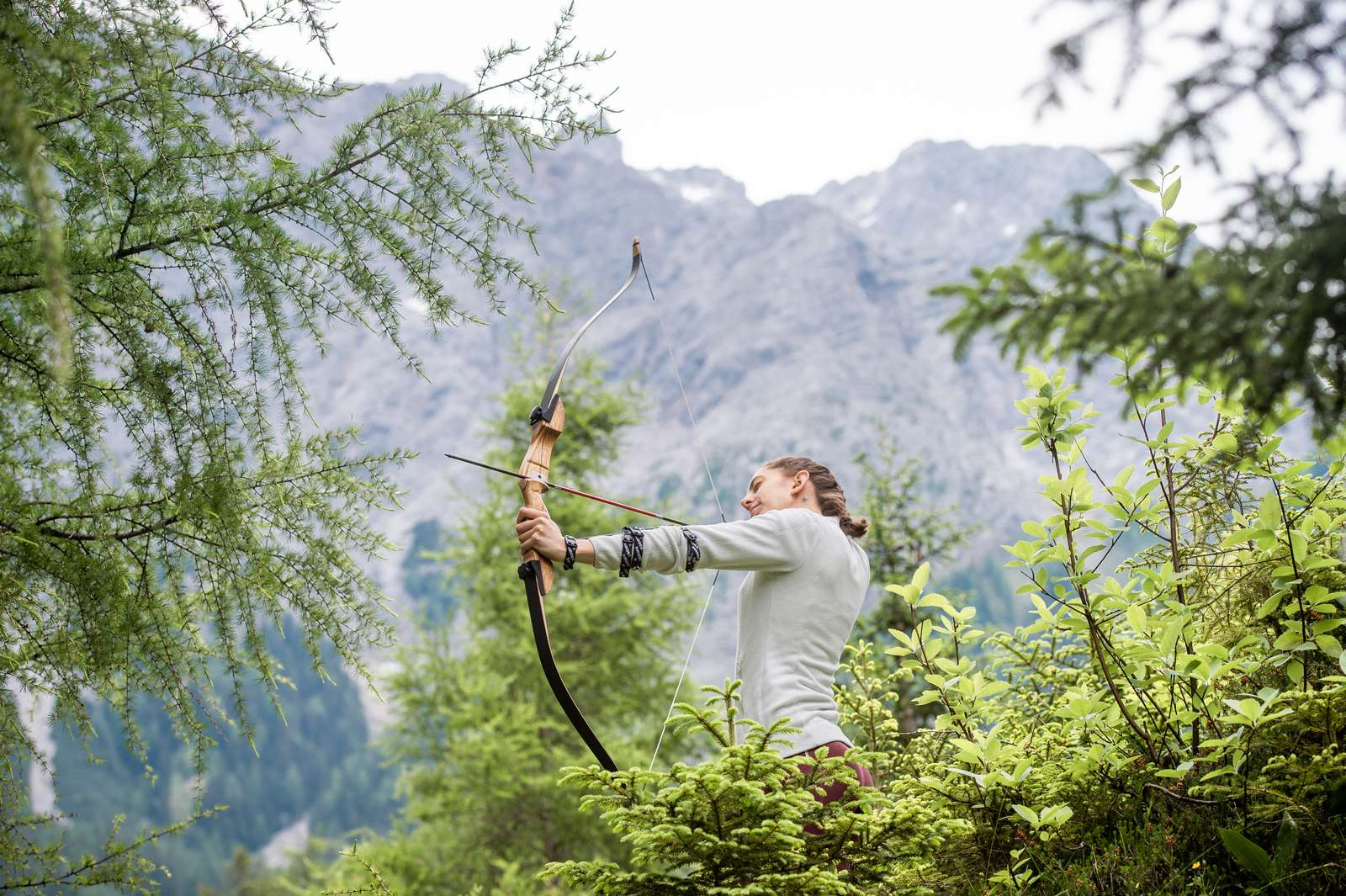 A woman strings an arrow on a bow, mountain panorama in the background