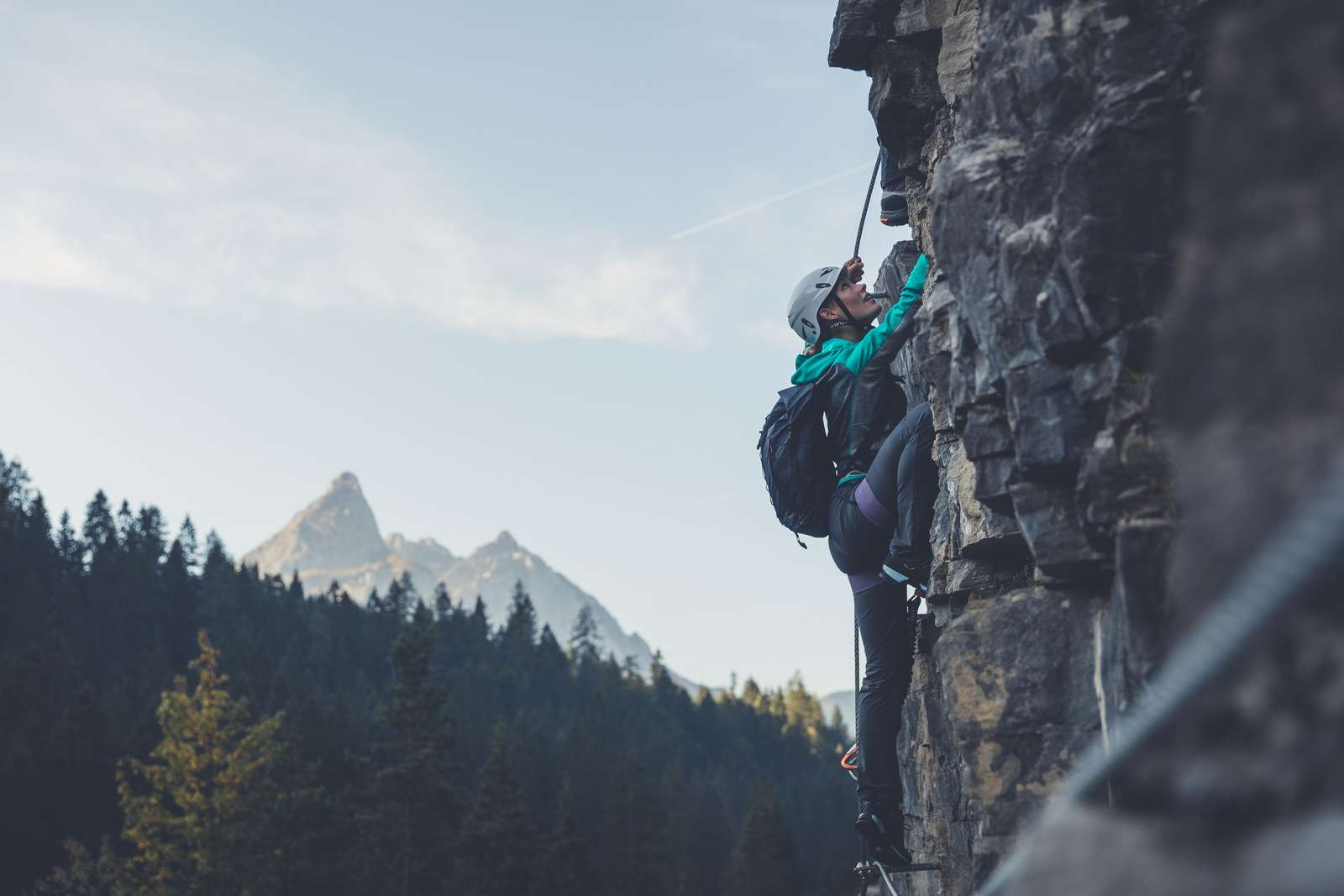 A woman wearing a climbing helmet and harness climbs a rock face