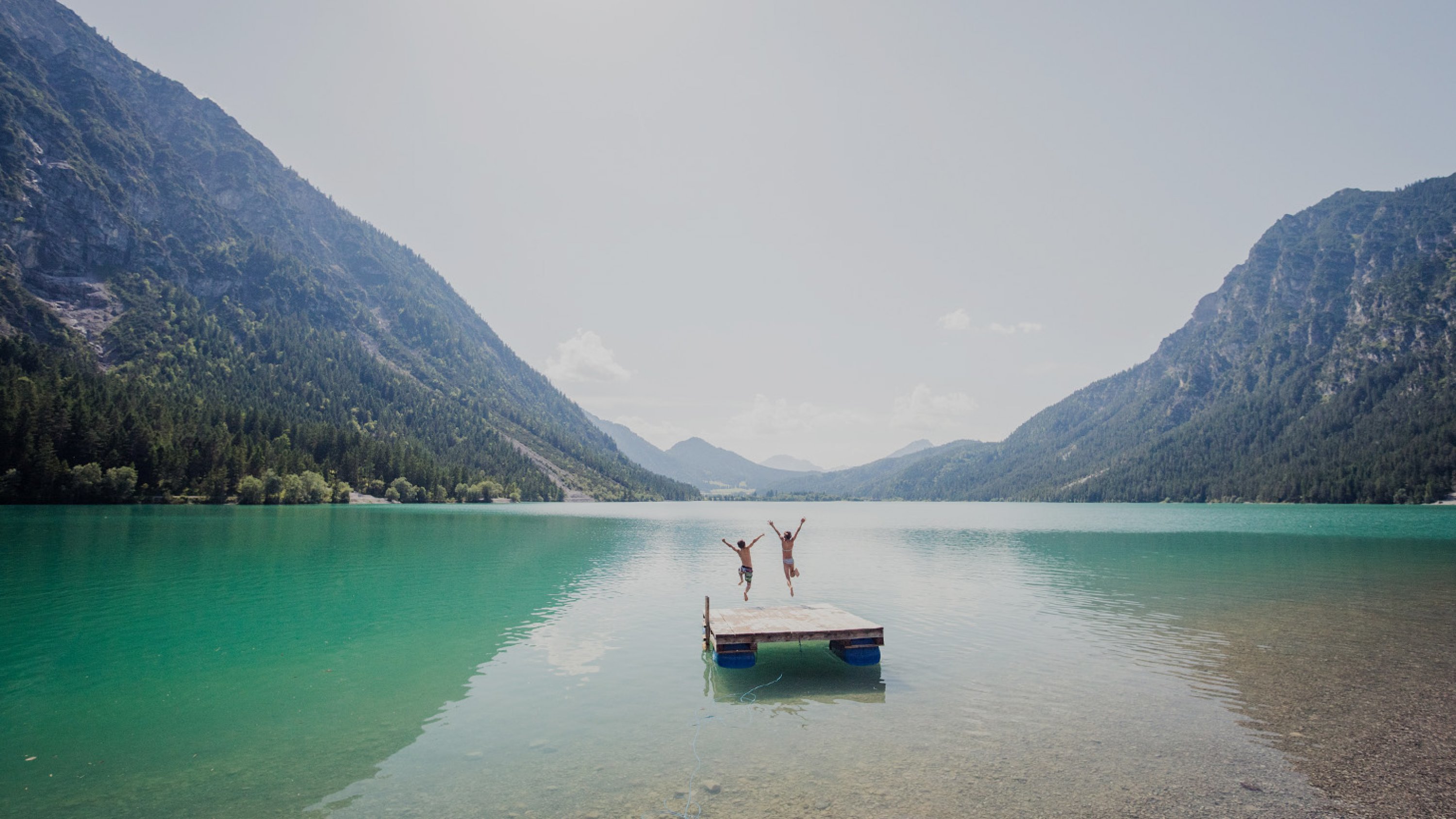 Heiterwanger See | TZA Zwei Kinder springen von einer Plattform in den türkisfarbenen Heiterwanger See