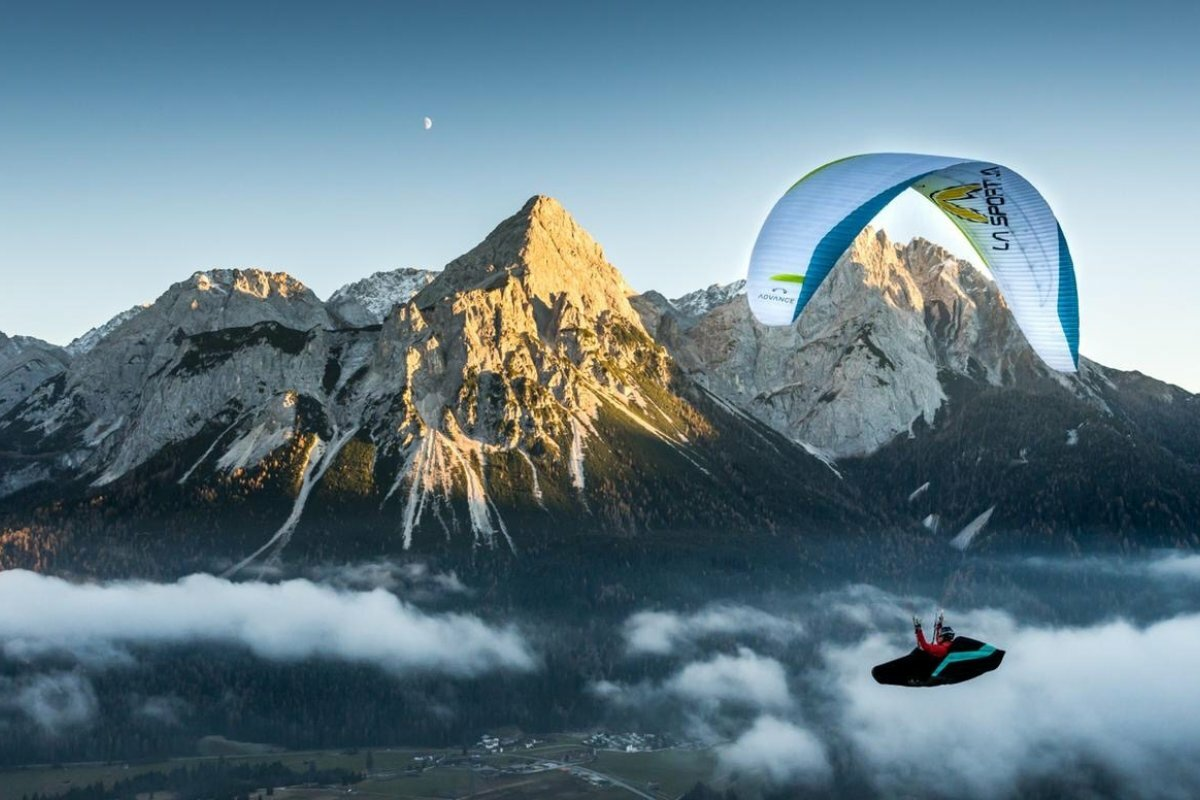 Ein Paragleiter fliegt über dem Tal und ein paar Nebelschwaden, im Hintergrund ein markantes Bergmassiv