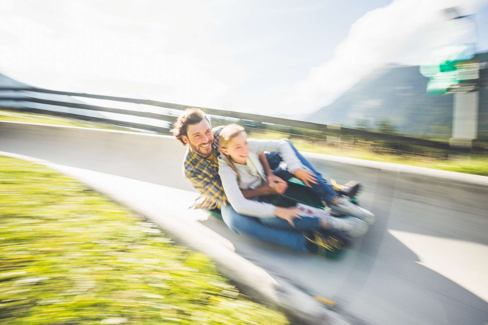 A man and a child ride together on a summer toboggan run and laugh