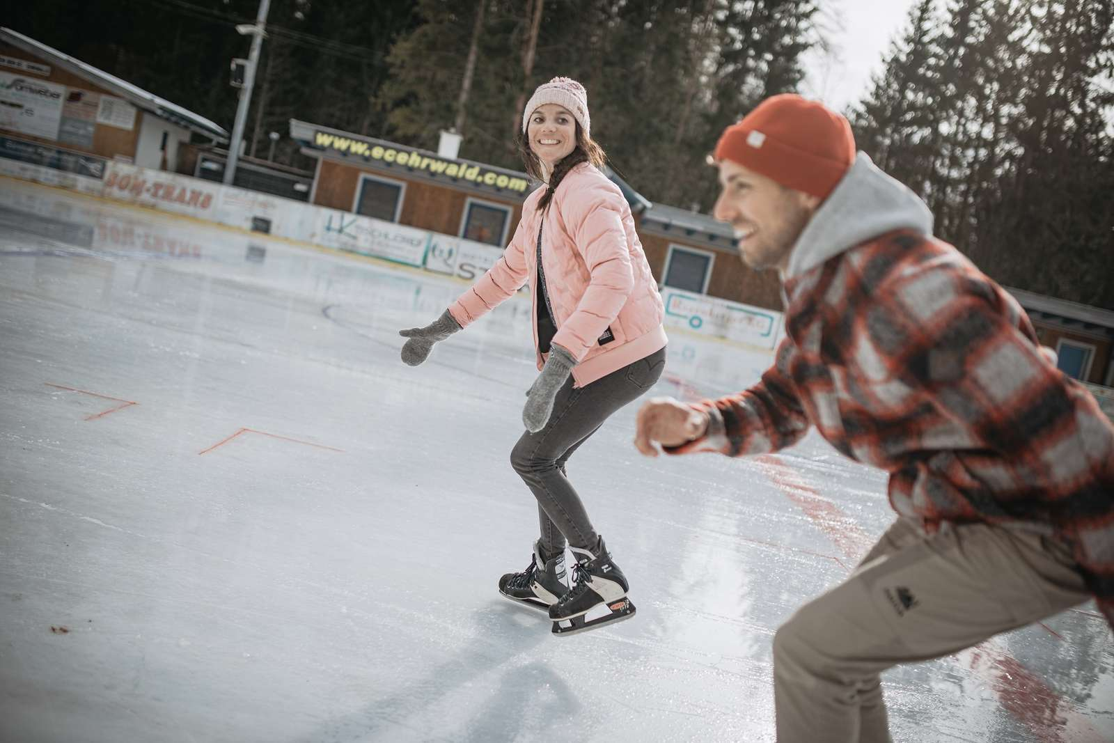 A woman and a man are skating on an ice skating rink