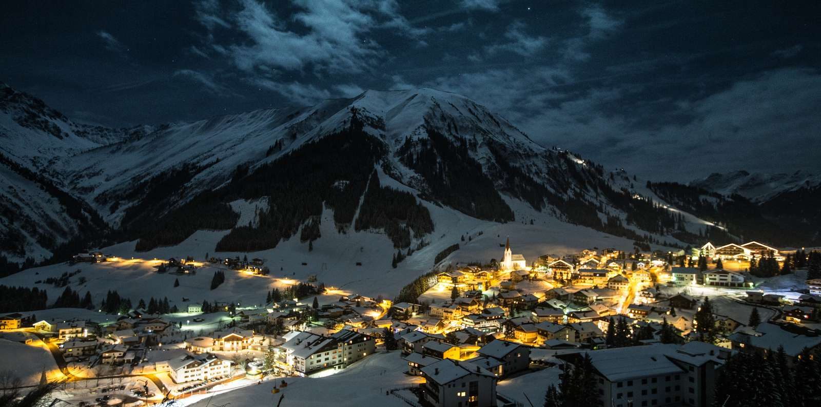 A winter landscape at night with a mountain panorama, an illuminated mountain village in the valley