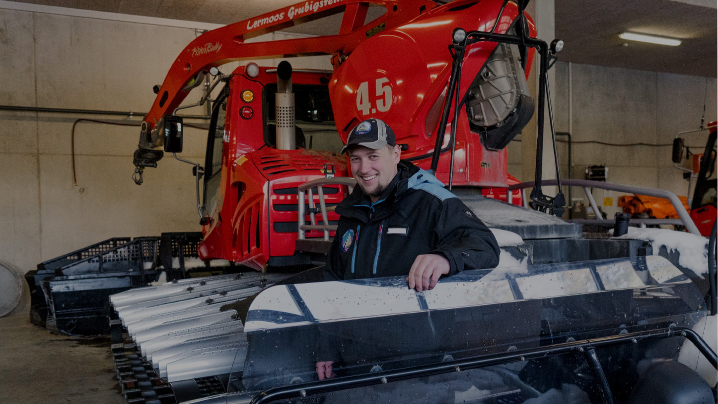 A Pistenbully driver stands in front of a red snow groomer